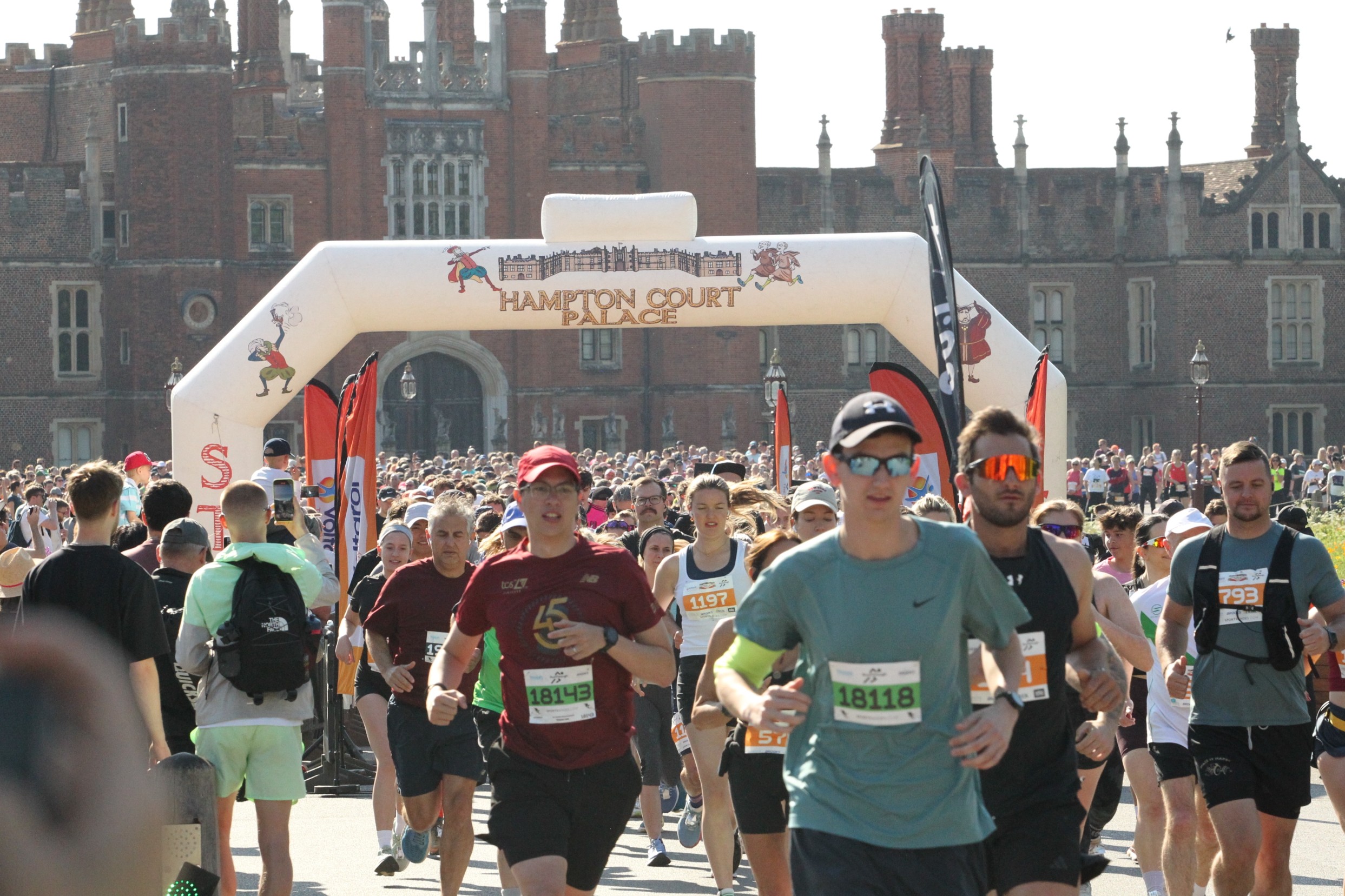 Runners taking part in the Hampton Court Palace Half Marathon, racing in front of the historic Hampton Court Palace on a sunny race day.